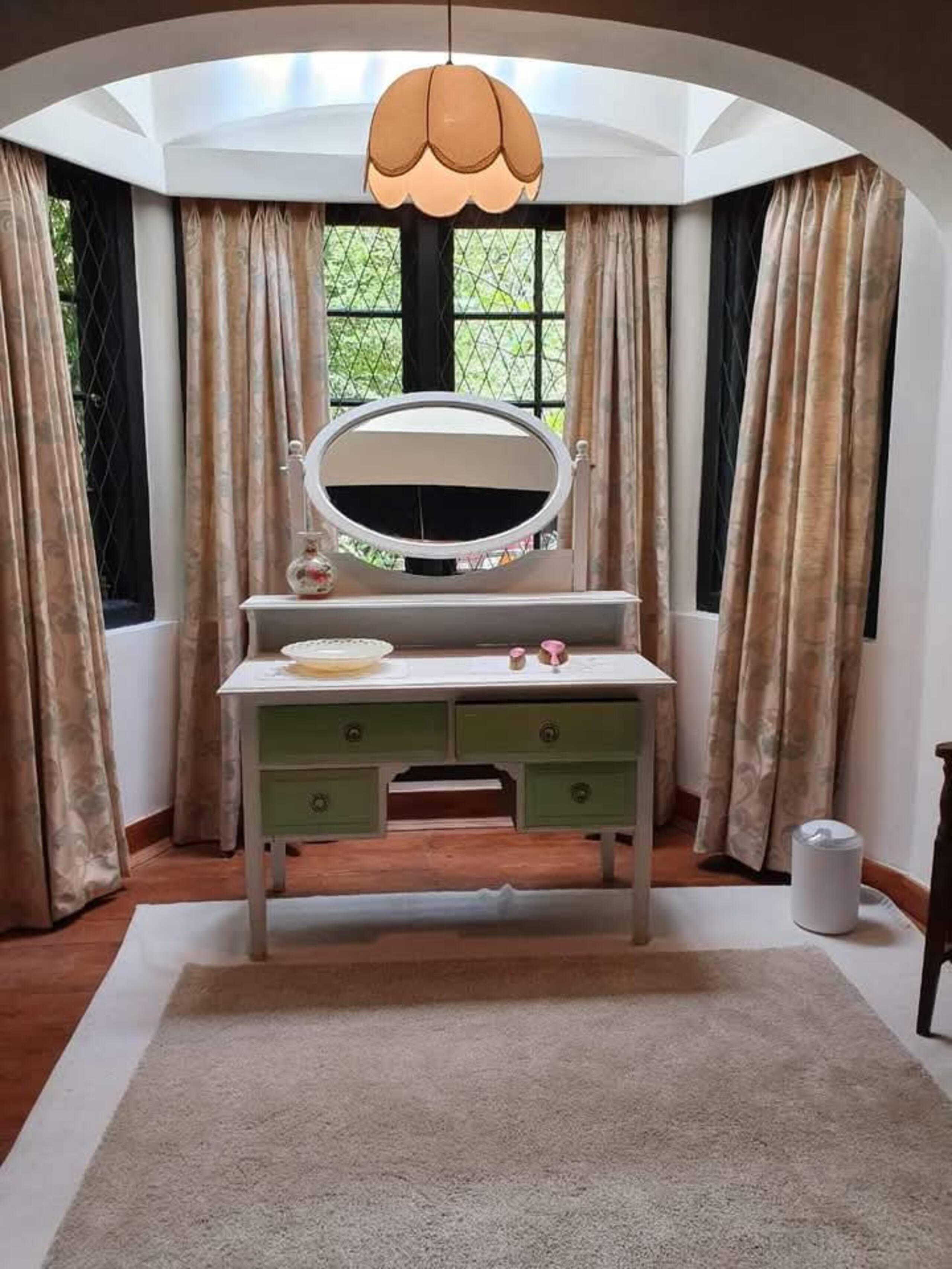 A vintage green dresser in a bedroom’s latticed bay window